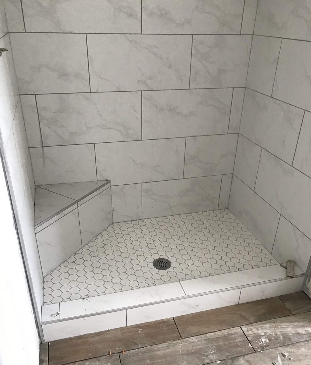 Finished marble-look shower with a hexagon mosaic pan and a built-in bench